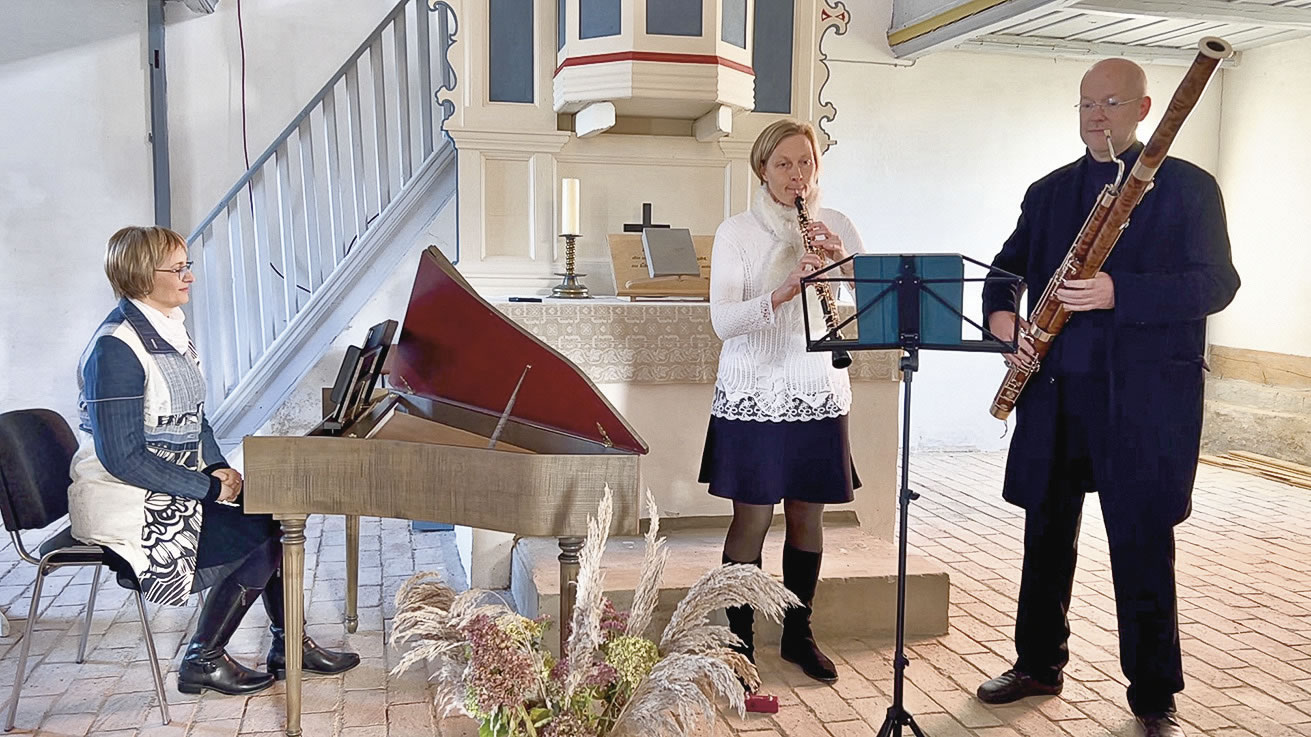 Die genannten Instrumentalist*innen (und Instrumente) in einem kleinen, alten, weiß-blau gestrichenen hölzernen Kirchraum.