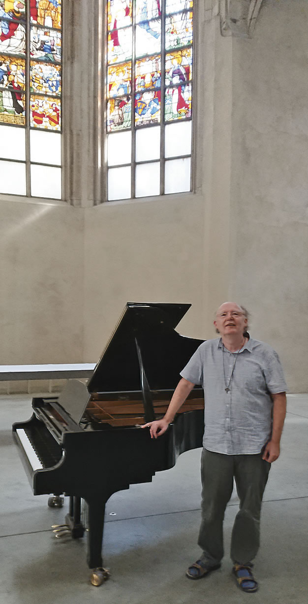 Ein Mann steht im blauen Hemd in einer Kirche vor einem Flügel.