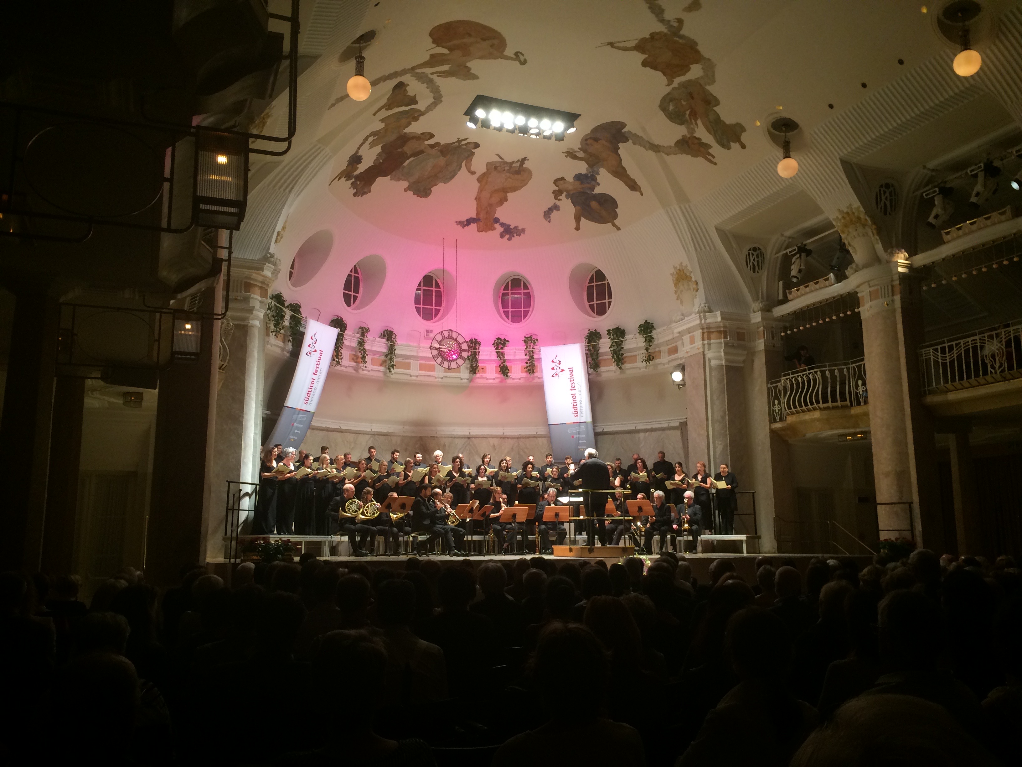 Über der Bühne eine rot angeschienene Kuppel. Auf der Bühne das Orchester.