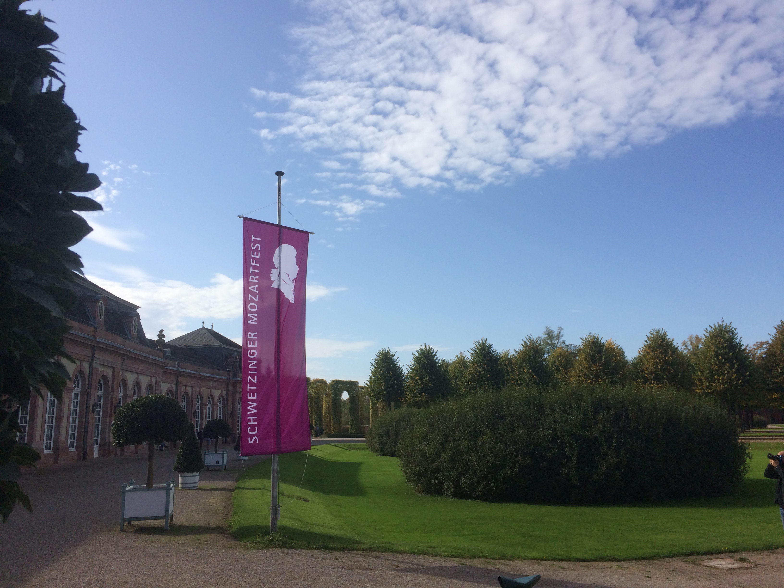 Das Mozartfest-Schwetzingen-Transparent nahe eines Kiesweges im Schlossgarten. Das Schloss im Hntergrund.