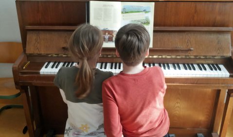 Zwei Kinder die sich eine Klavierbank teilen und an der Klaviatur spielen.