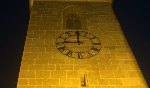 Die Uhr am dunkelgelb erleuchteten Kirchturm zeigt 9:00 Uhr.