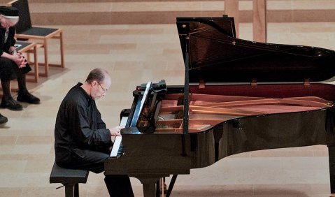 Ein Mann in schwarz mit kurzem Haar sitzt kontemplativ spielend am Konzertflügel.