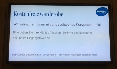 Bildschirm: "Kostenfreie Garderobe Wir wünschen Ihnen ein unbeschwertes Konzerterlebnis! Bitte geben Sie Ihre Mäntel, Taschen, Schirme etc. kostenfrei bei uns im Eingangsfoyer ab."