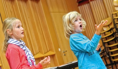 Nahaufnahme von zwei Kinder die in einem Holzvertäfelten Saal singen.