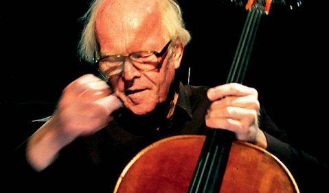 Ein Cellist gehobenen Alters. Das Foto zeigt ihn mit wenigen weißen Haaren, in dunkler Kleidung und mit dem Bogen energisch gestikulierend oder dirigierend.