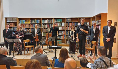 Die gemischten Instrumentalist*innen stehen in der Bücherei schwarzgekleidet zum Applaus zusammen.